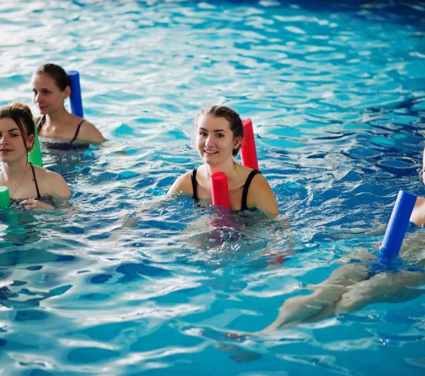 Fitness group of girls doing aerobical excercises in swimming pool at aqua park. Sport and leisure activities.